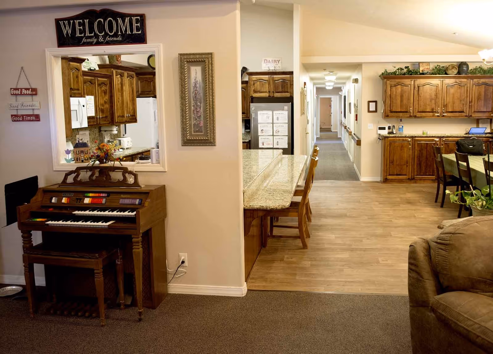 Warmly furnished interior common area showing an organ, a kitchen island with stools, a dining area and a hallway.