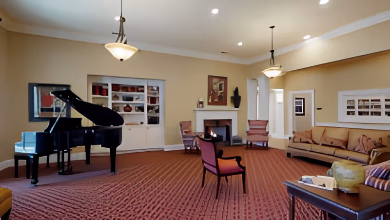 Spacious common room with a grand piano, fireplace and multiple seating areas under warm lighting.