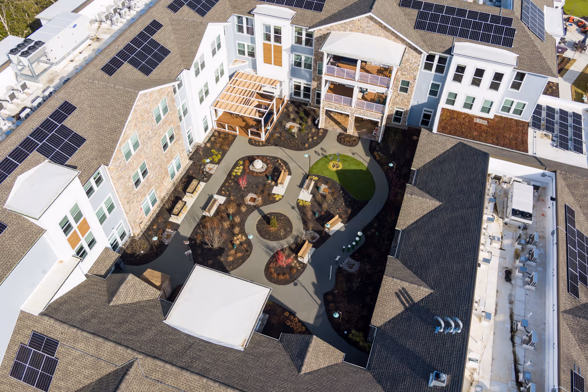 Aerial view of a senior living facility's central courtyard with winding paths, benches, landscaping, and surrounding buildings with solar panels.