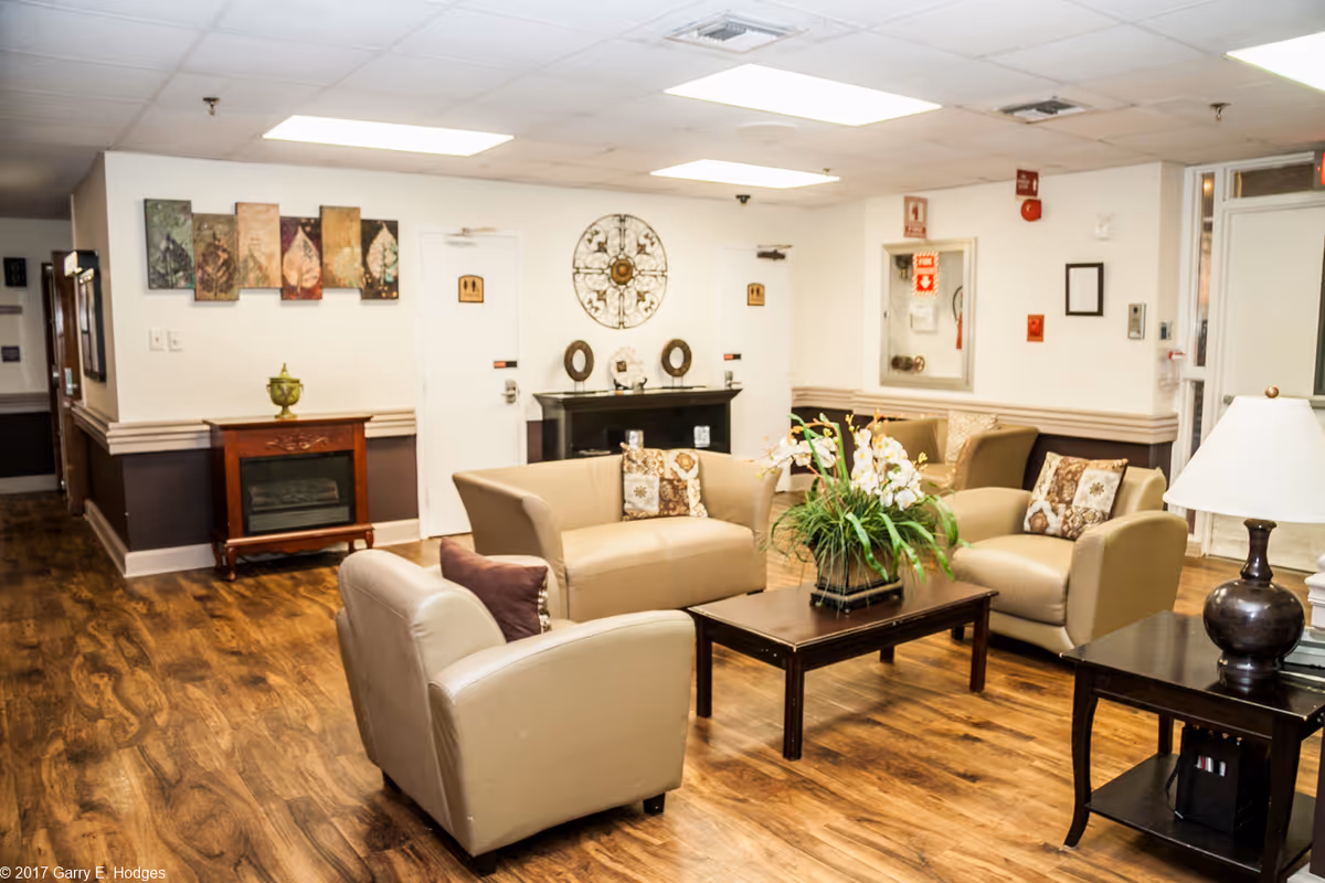Well-lit lounge with beige sofas and armchairs arranged around a central coffee table with a plant.
