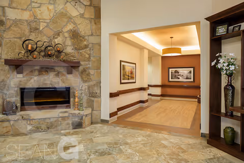 Cozy common area with a stone fireplace, tiled floor, hallway and decorative shelving with vases.