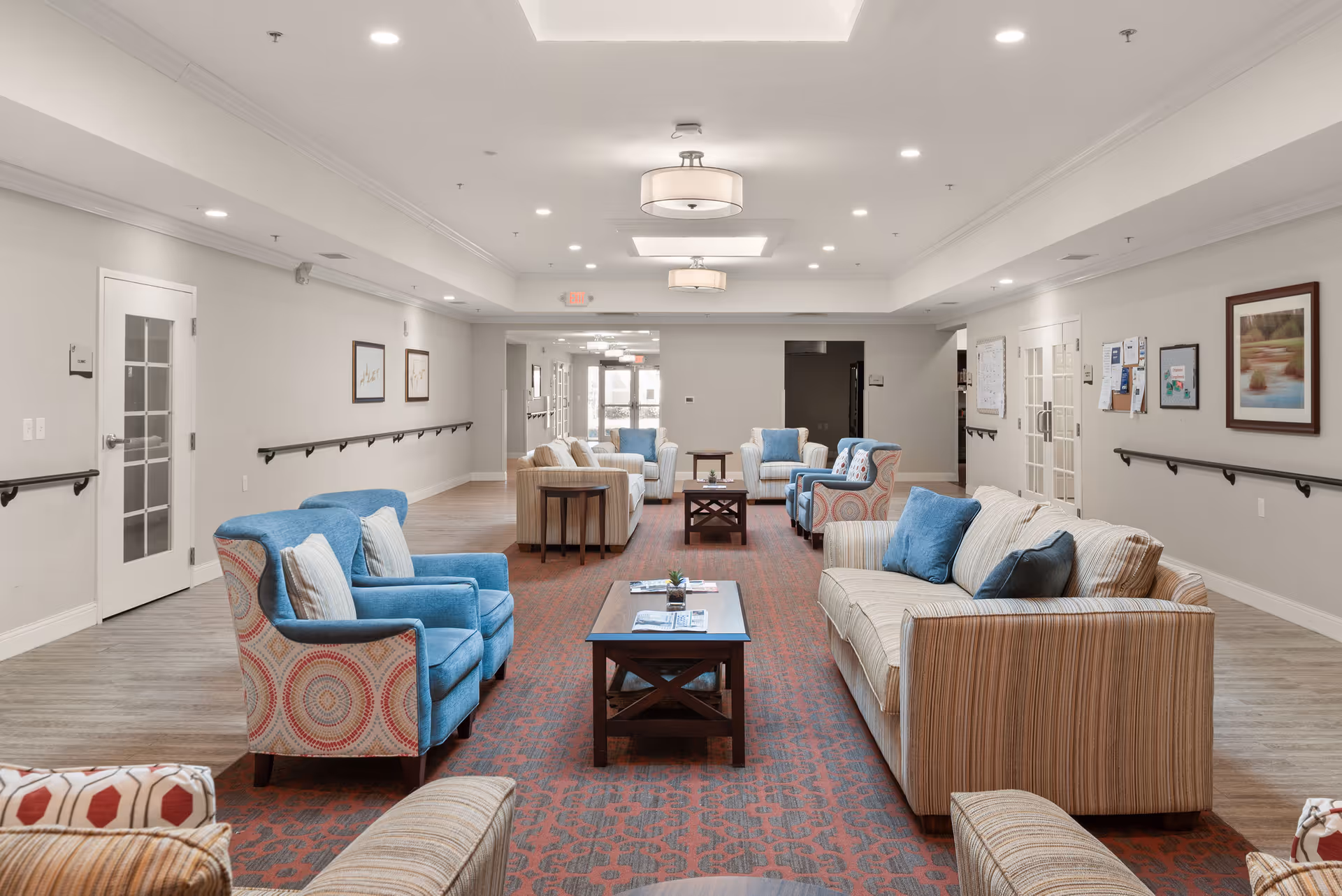 Bright communal living room with sofas and armchairs arranged around coffee tables in a senior living facility.