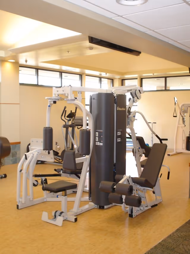A bright indoor fitness room with a multi-station weight machine and other exercise equipment.