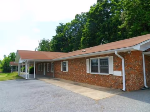 Brick, single-story Serenity Care facility with a covered walkway and surrounding green trees.