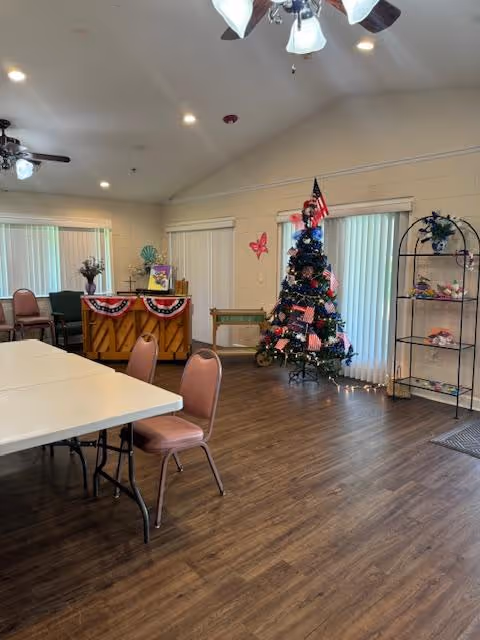 Community activity room with folding tables and chairs, a decorated Christmas tree, piano, and display shelves.