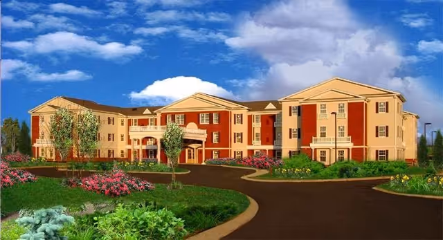 Three-story red-and-beige senior living building with landscaped grounds and a circular driveway under a blue sky.