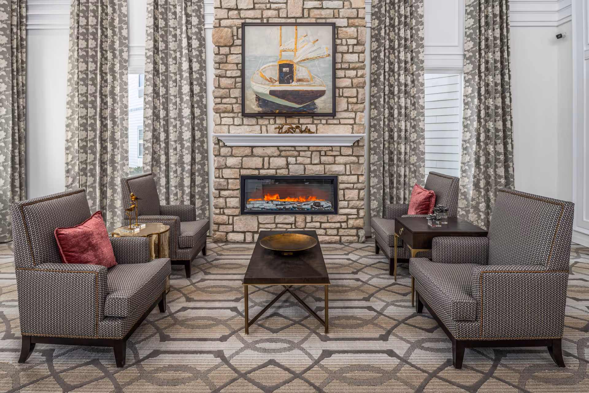 Cozy seating area with four upholstered armchairs around a coffee table facing a stone fireplace topped by a framed painting.