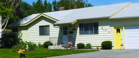 Front view of a pale green, single-story house with a yellow door and lawn.