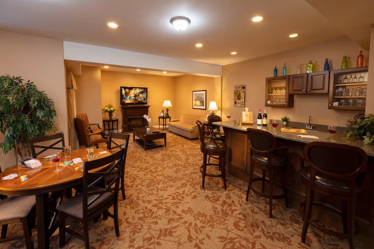 Cozy senior living common room with a bar, high stools, dining table, sofa seating and a TV.