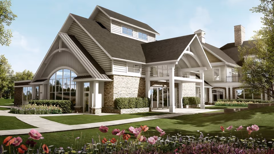 Exterior view of a senior living facility building with a modern design featuring large windows, stone and siding walls, a covered entrance, and well-maintained landscaping with green lawns and colorful flowers in the foreground.