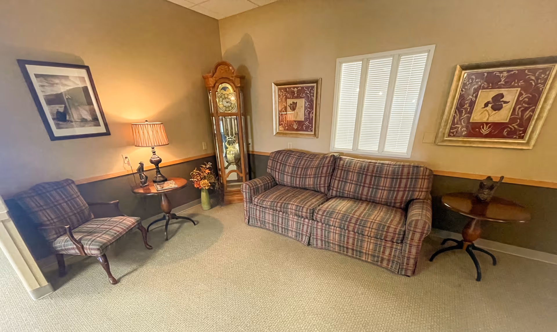 Cozy living room at Meadowbrook Place with plaid sofa, chairs, tables, and a grandfather clock.