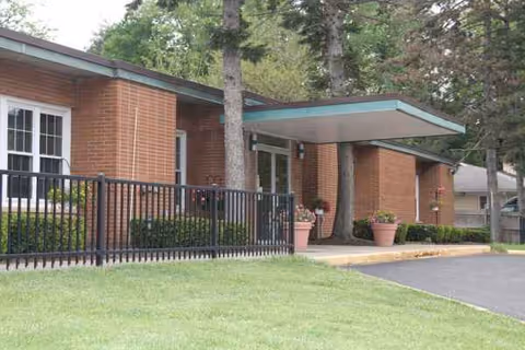 Brick senior living facility with a covered entrance, railing, and potted plants.