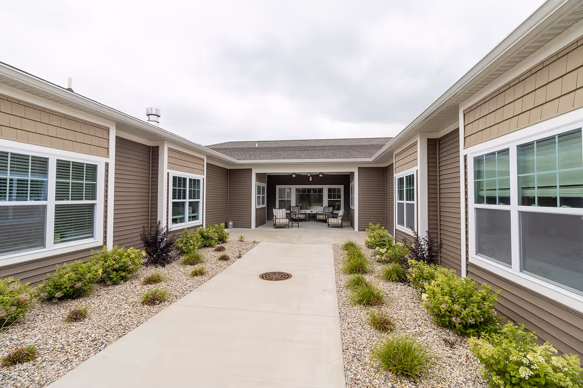 Paved courtyard between single-story brown-sided wings leading to a covered seating area with chairs.