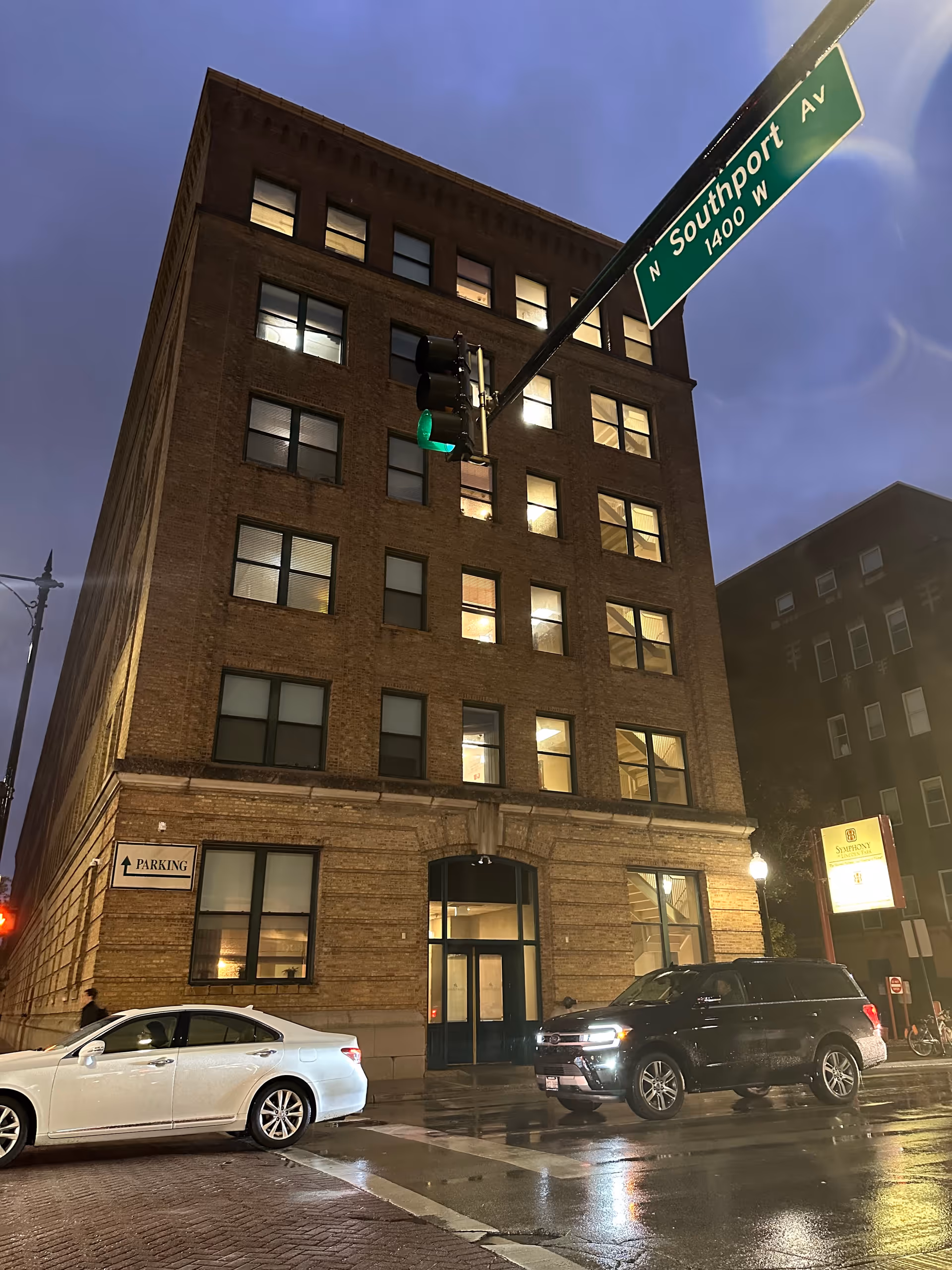 Multi-story brick building front at a rainy intersection at night with cars parked and a 'N Southport Av' street sign overhead.