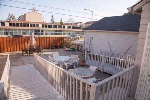 Outdoor patio at Hacienda Place with white tables, chairs, umbrella, and potted plants.