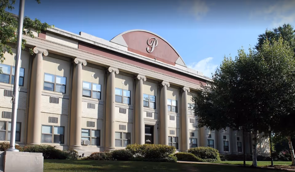 Front facade of a large, classical-style building with tall columns and a curved emblem.