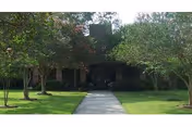 Tree-lined walkway leading to the front entrance of a low brick building with a manicured lawn.