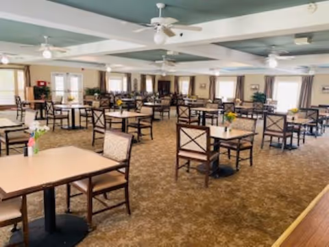 Spacious dining room with multiple tables and chairs, ceiling fans, and windows along the walls.