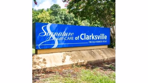 Blue and white outdoor sign for Signature HealthCARE of Clarksville located at 198 Old Farmers Road, surrounded by greenery and trees.