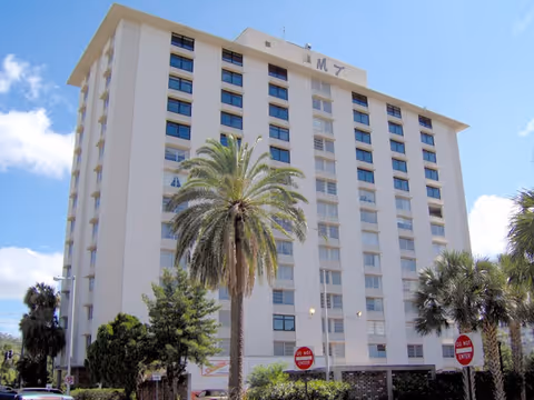 A tall white multi-story senior living building with palm trees in the foreground.
