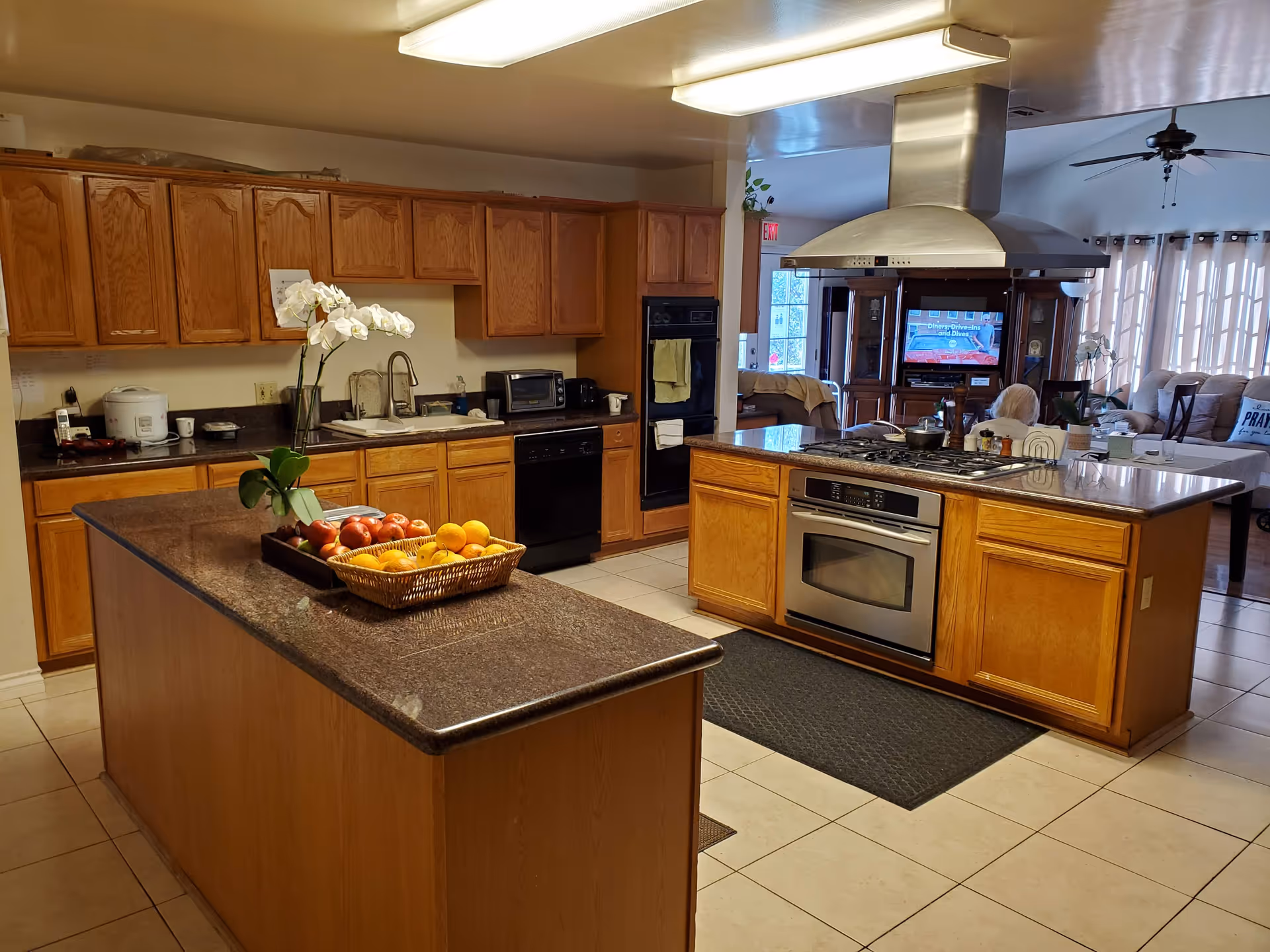 Large open kitchen with two islands, wooden cabinets, a stainless steel oven and range hood, and a basket of fruit on the counter.
