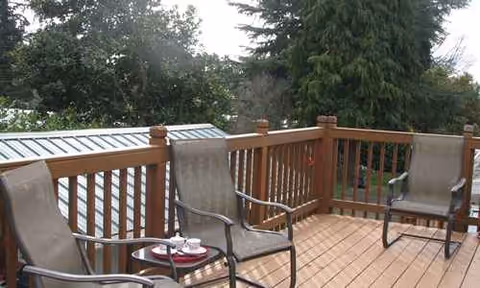 Outdoor wooden deck with chairs and a small table surrounded by trees