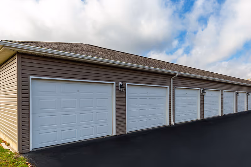 A row of attached white garage doors on a single-story building under a cloudy sky.
