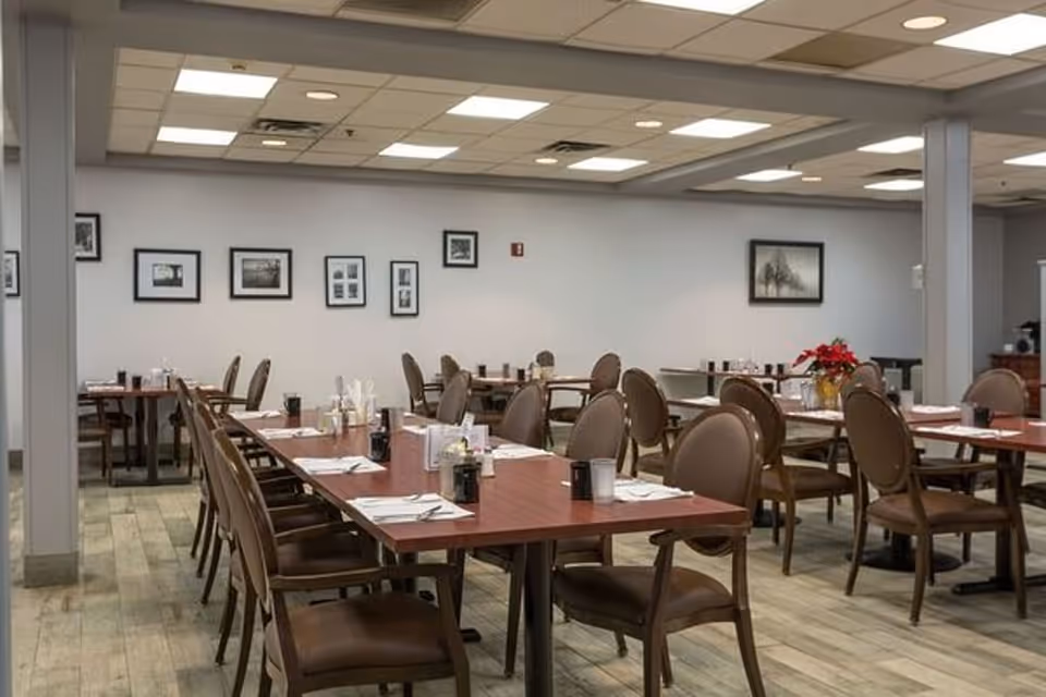 Spacious dining room with rows of tables and brown chairs set for meals and framed pictures on the wall.