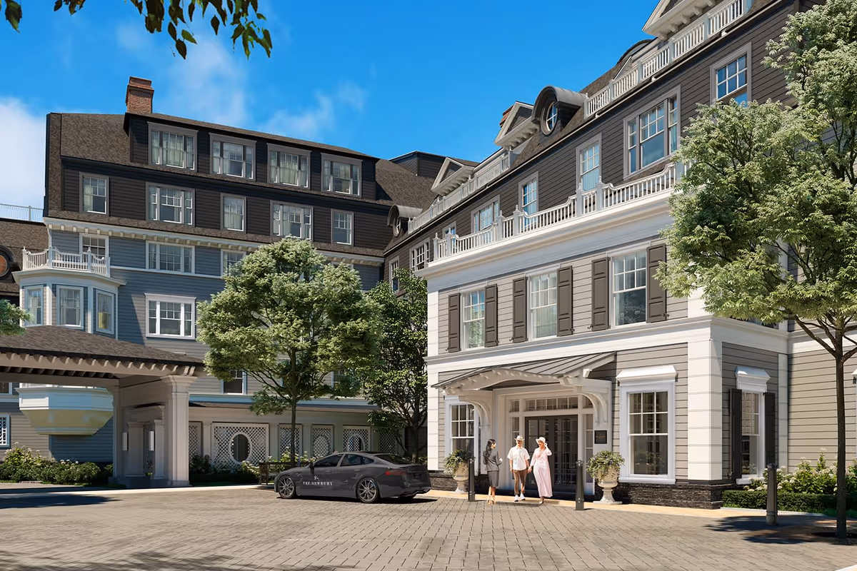 Exterior view of The Newbury Of Brookline senior living facility showing a large, multi-story building with classic architectural design, trees, and a paved driveway. Three people are standing near the entrance, and a black car with 'The Newbury' logo is parked nearby.