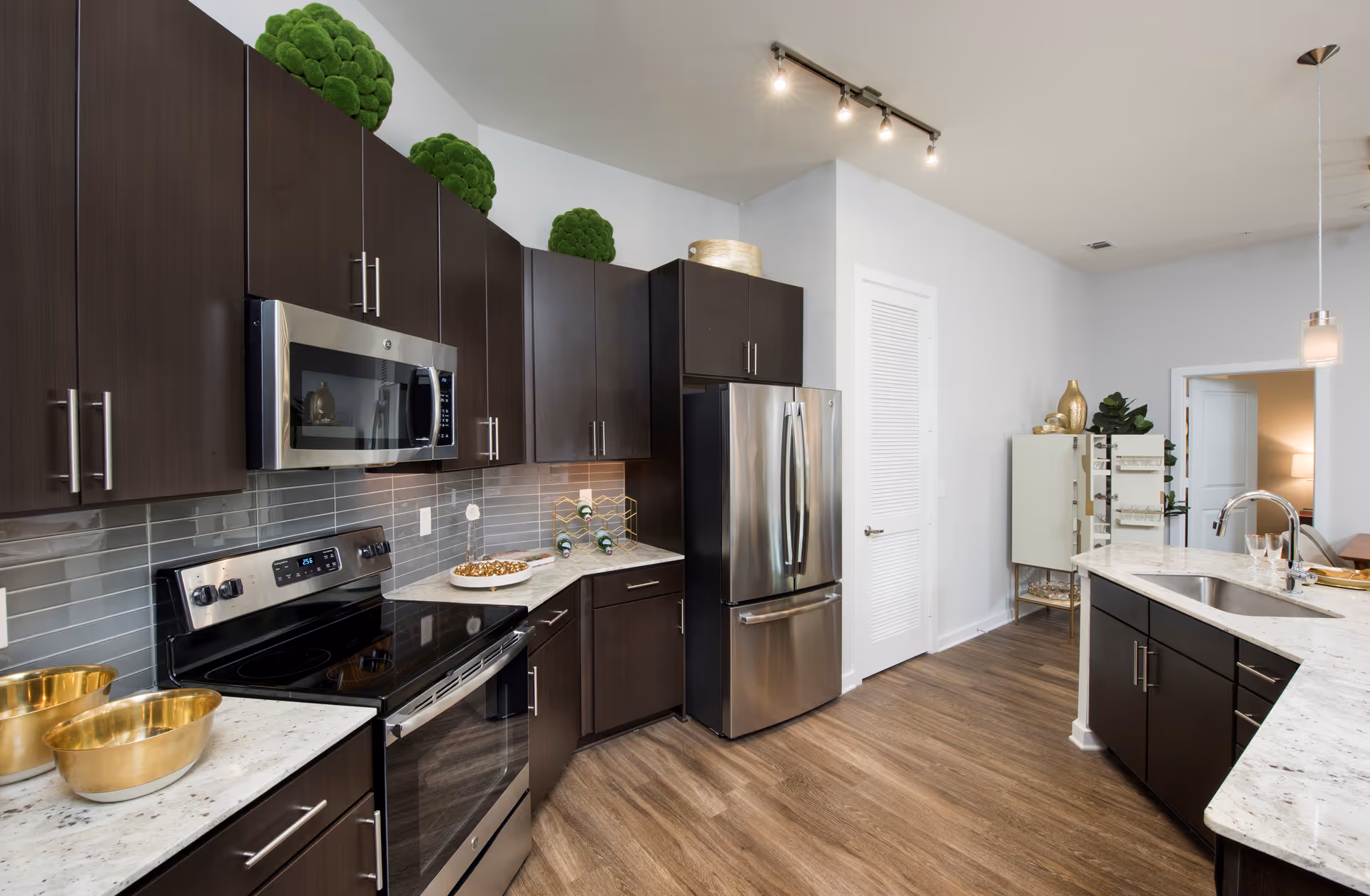 Contemporary kitchen with dark cabinets, stainless steel appliances, marble countertops, and a central island with sink.