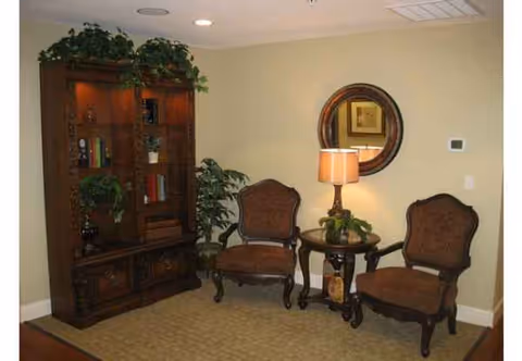 Cozy living room seating area with two chairs, lamp, round mirror, and bookshelf.