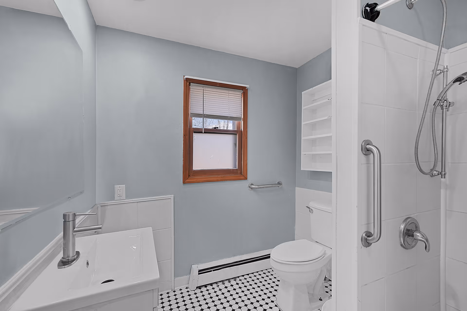 Small bathroom with a sink, toilet, tiled walk-in shower with grab bars, and a window.