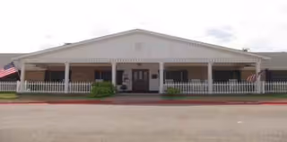 Front exterior of Keeneland Nursing & Rehabilitation with a covered porch, railing, and flags.