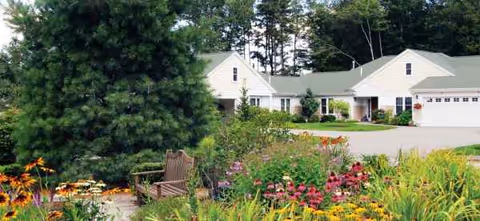 White-fronted senior living facility with landscaped garden and bench in foreground.
