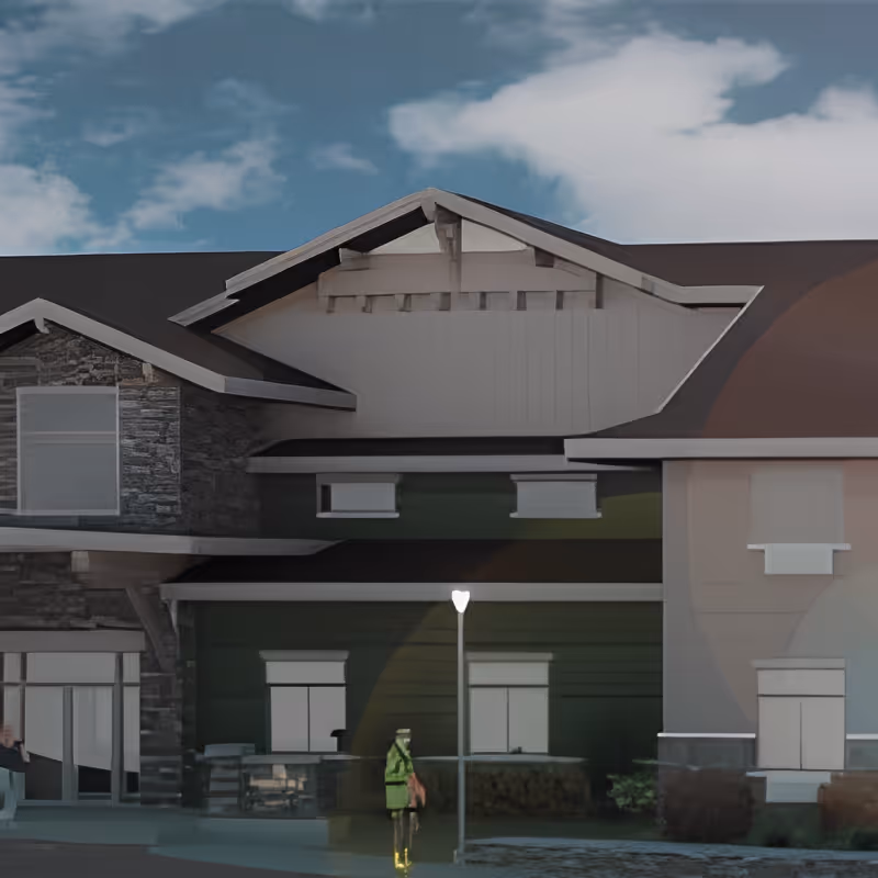 Front exterior of a multi-story building with gabled roofs, mixed stone and siding facade, a lit lamppost, and a person near the entrance.