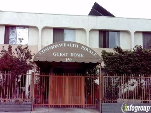 Exterior view of Commonwealth Royale Guest Home, a two-story building with a gated entrance and an awning displaying the facility's name and address number 150. The building is surrounded by trees and bushes.