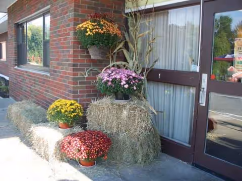 Exterior view of a nursing home entrance with hay bales and potted flowers.