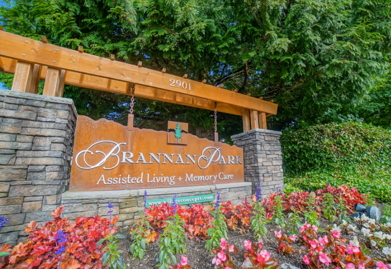 Outdoor entrance sign for Brannan Park Assisted Living + Memory Care, mounted on a stone and wood structure surrounded by colorful flowers and greenery.