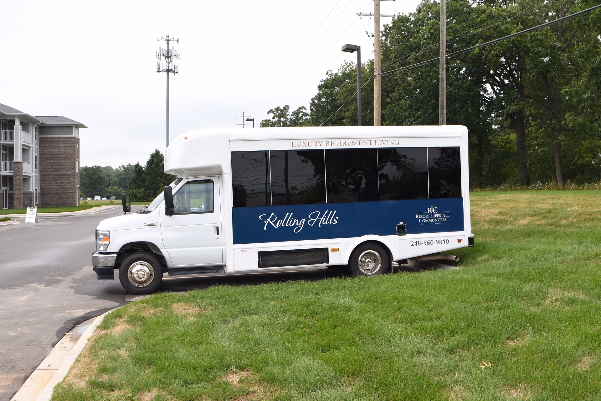 A white and blue Rolling Hills retirement community shuttle bus parked on grass outside a residential building.