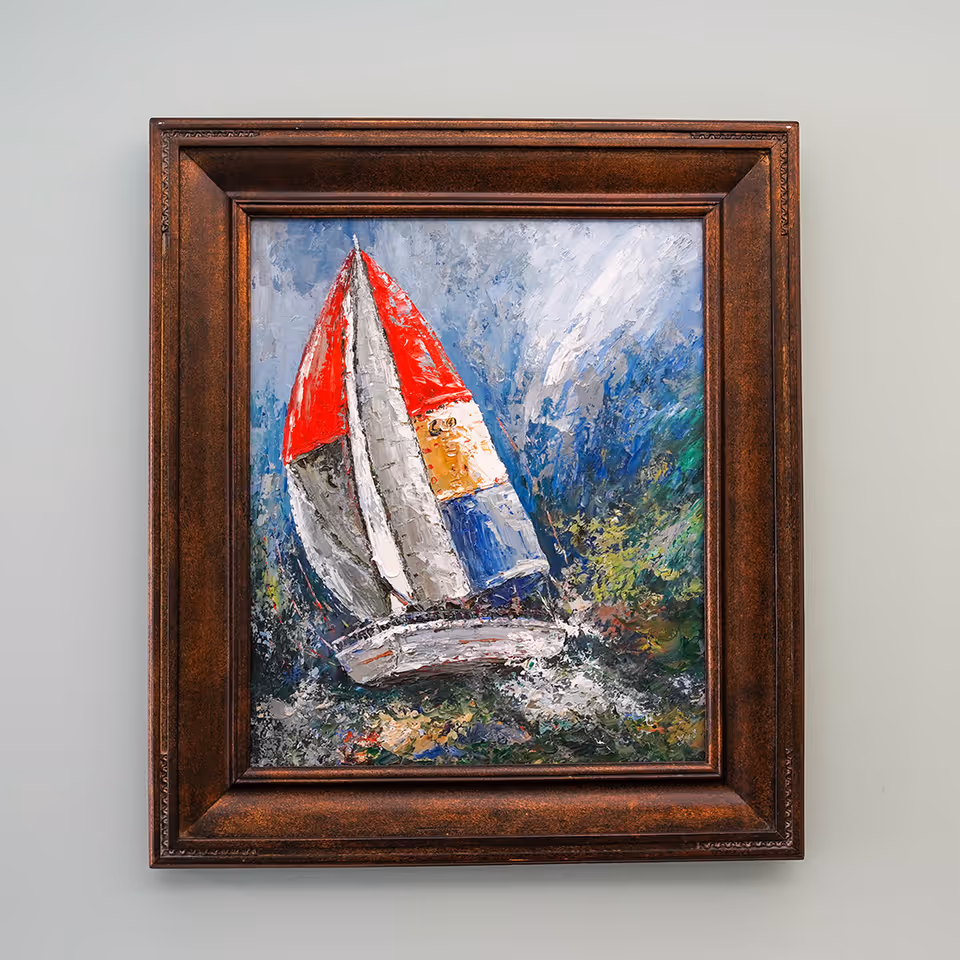 A framed painting of a sailboat with a red, white, yellow, and blue sail on a textured, colorful background, hanging on a light gray wall.