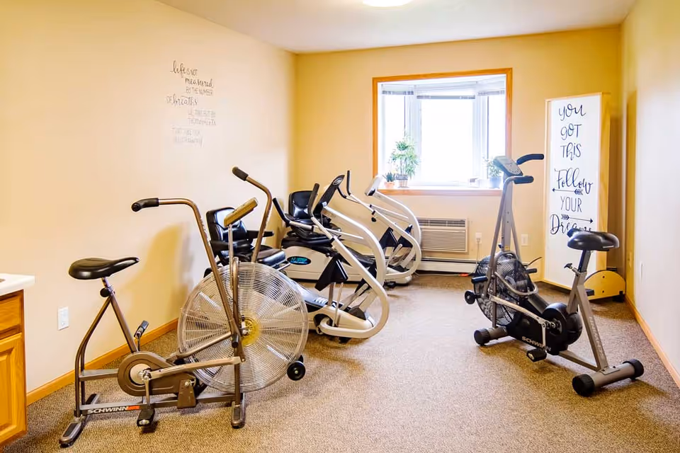 Small exercise room with several stationary and recumbent bikes, a window, and a motivational sign on the wall.