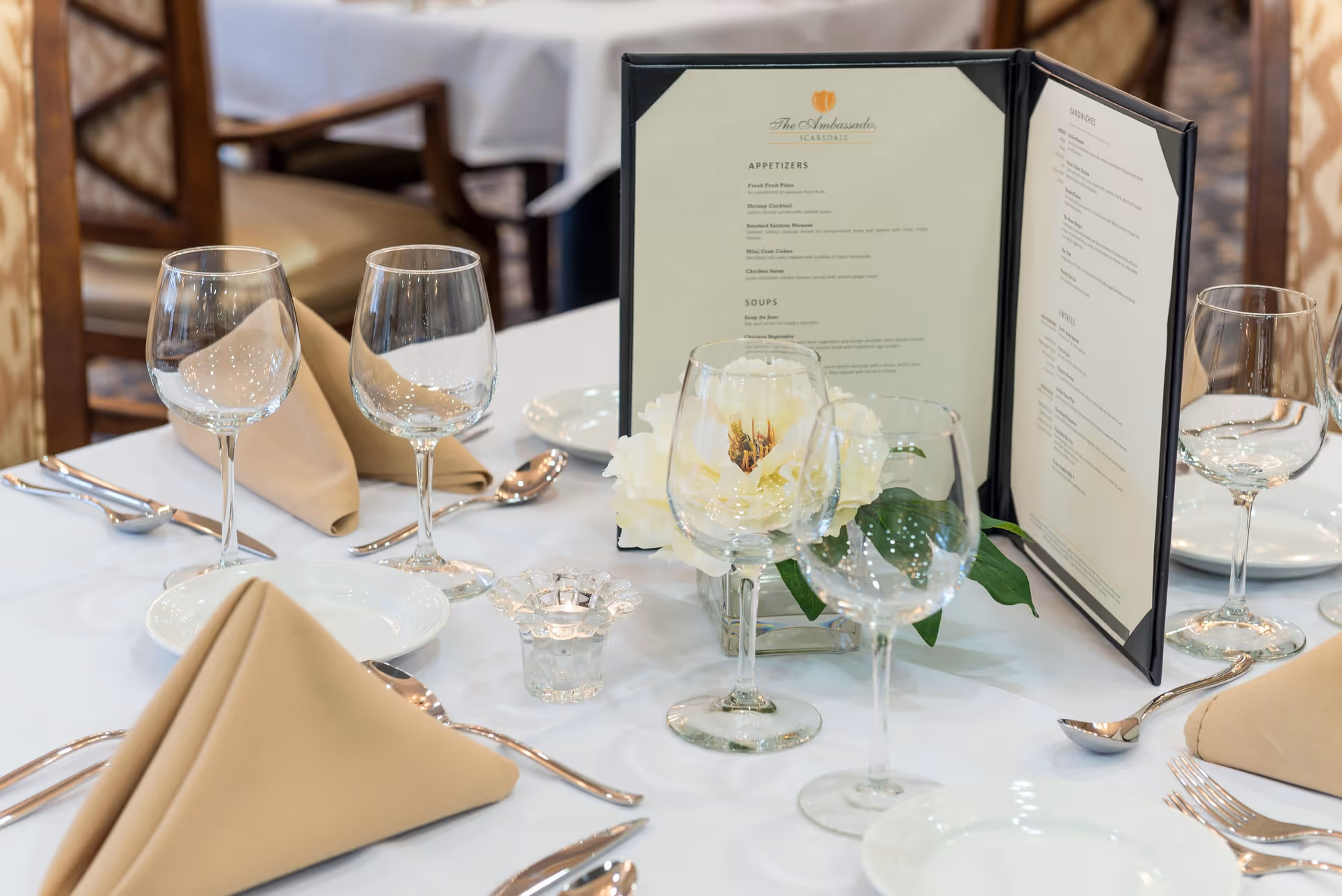 Elegantly set dining table with folded napkins, wine glasses, a menu and a floral centerpiece.