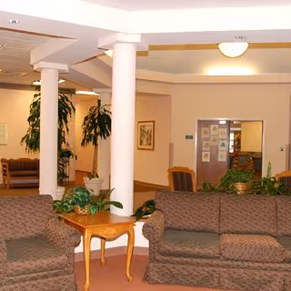 Lobby-style common area with upholstered sofas, a wooden side table, white columns, and indoor plants.