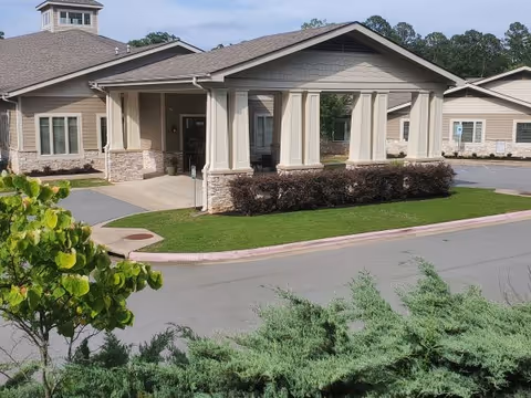 Covered porte-cochère entrance of a single-story senior living building with columns, stone accents, landscaped beds and a driveway.