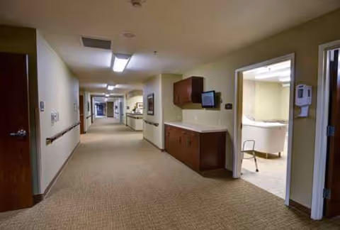 Long beige hallway in a nursing center with a kitchenette area along the right.