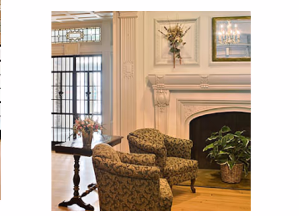 Elegant living room in a senior facility with patterned chairs, a fireplace, and a plant.