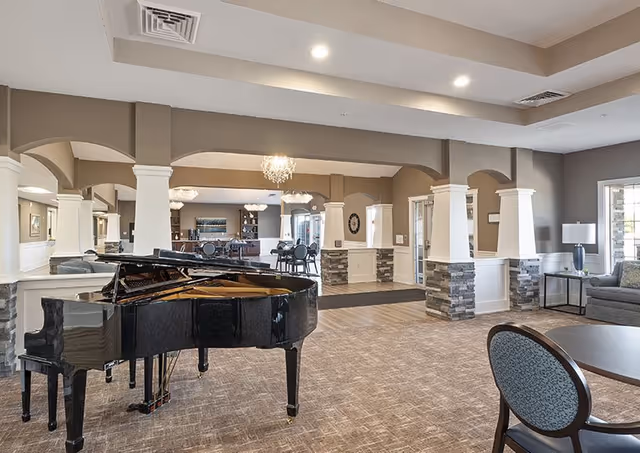 Spacious senior living common area with a grand piano, seating, columns, and chandeliers.