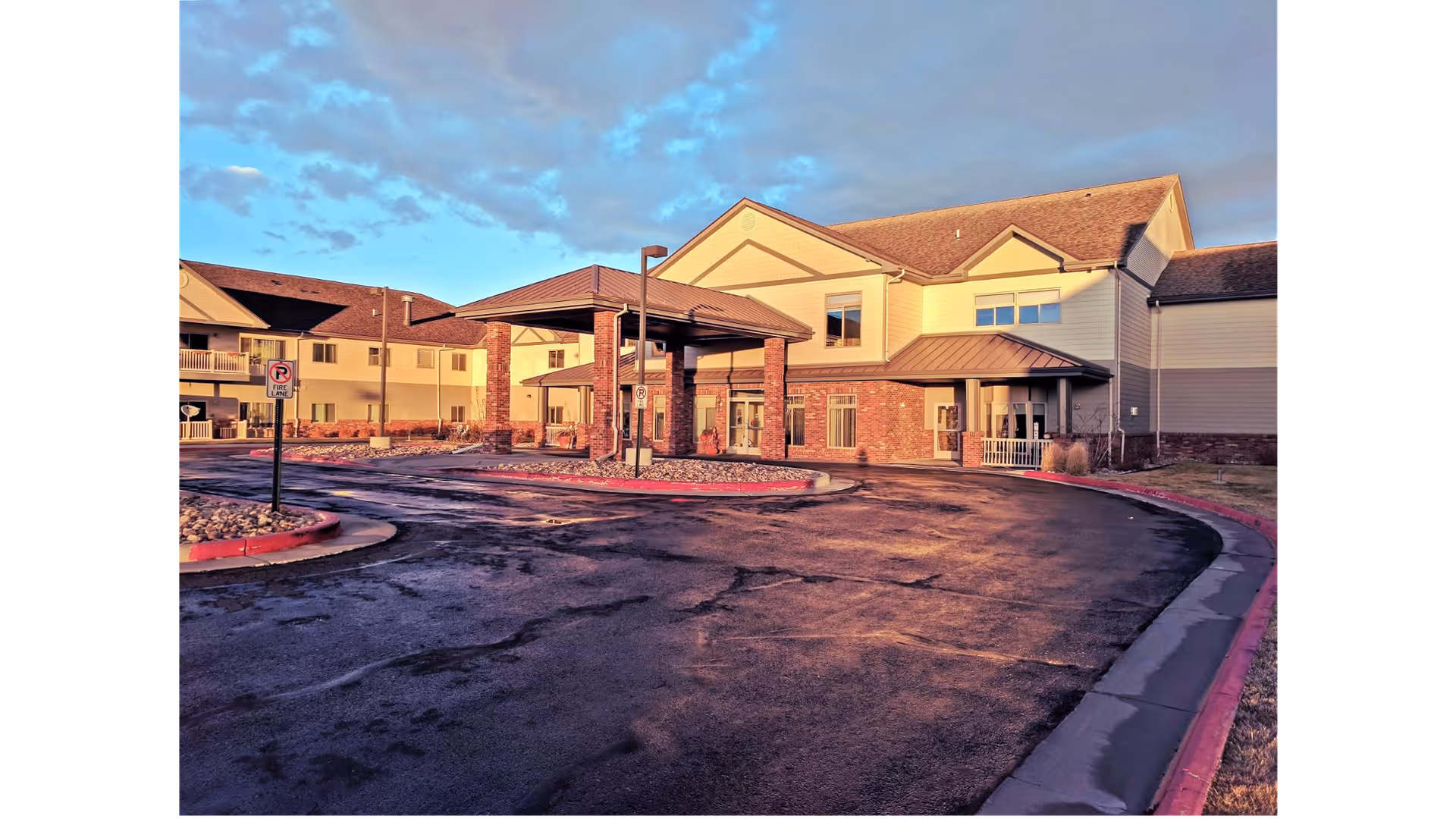 Exterior view of Primrose Retirement Community of Casper building during sunset with a covered entrance and a curved driveway in front.