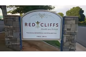 An outdoor entrance sign reading 'Red Cliffs Health and Rehab' mounted between stone pillars with trees and pavement in the background.