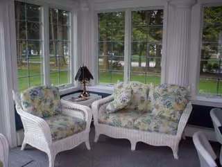Sunlit wicker seating area with floral cushions inside a glass-walled sun porch.